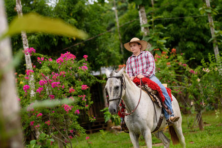 Photo of a young Peruvian farmer riding a horse. Trees and shrubs in the backdrop
